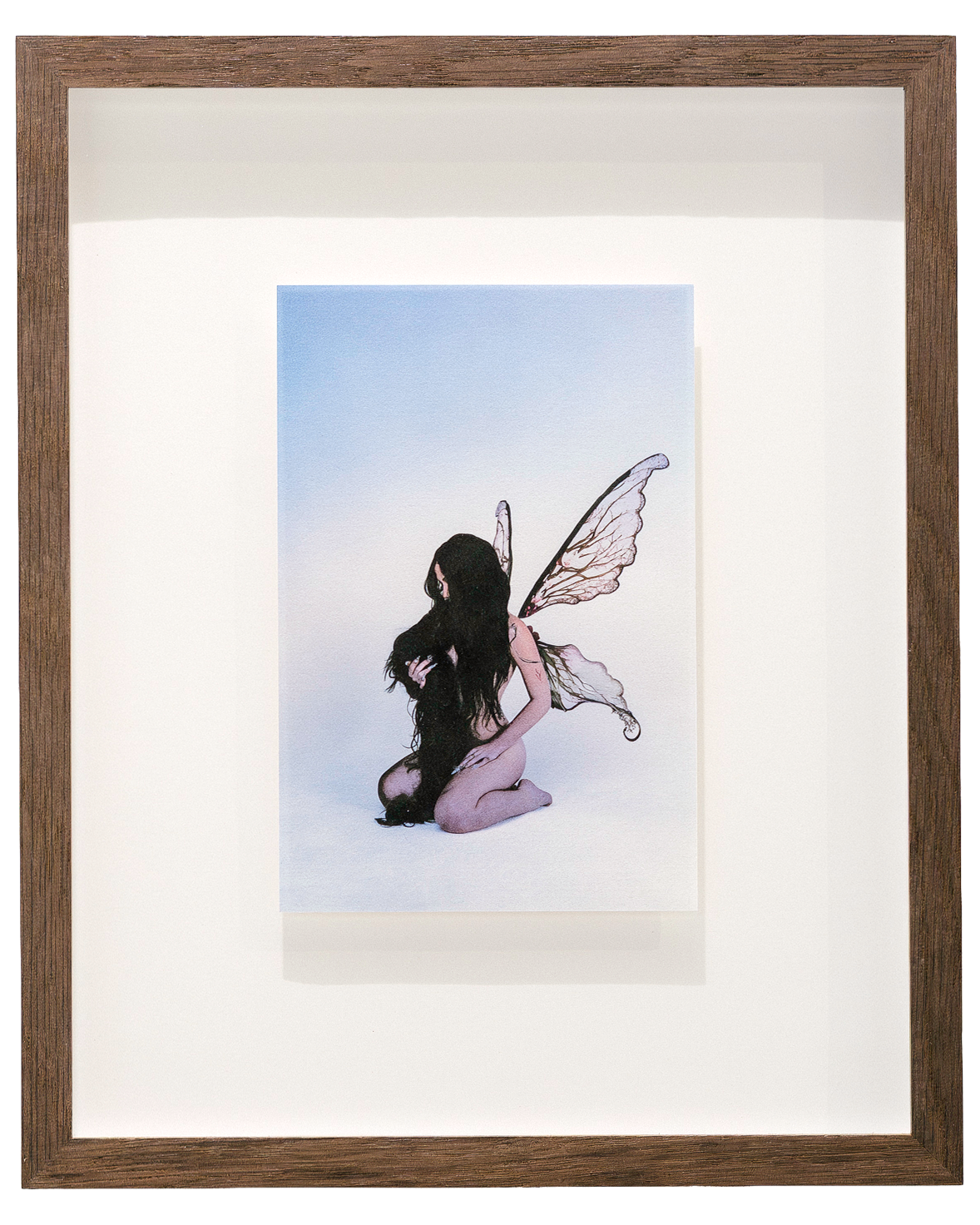 Fine art photograph by Alaïa Fonk of a kneeling woman with long dark hair and delicate fairy wings against a soft blue background.